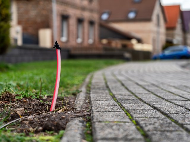 Ein rotes Kabel ragt am Rand eines Gehwegs aus dem Boden.